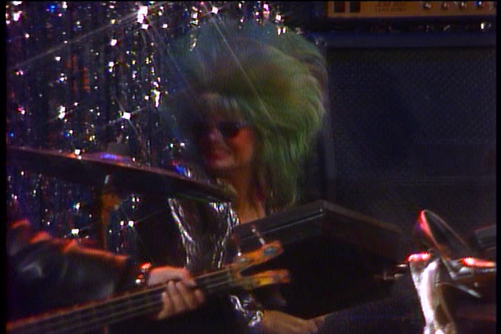 Blair plays the drums with a big green bouffant.